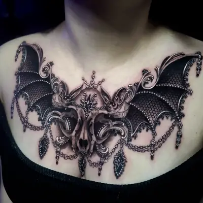 Chest tattoo featuring bat wings, skulls, and ornate jewelry design.