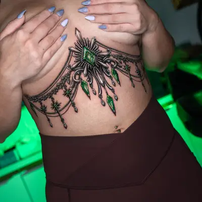 Tattoo of ornate jeweled design under breasts.