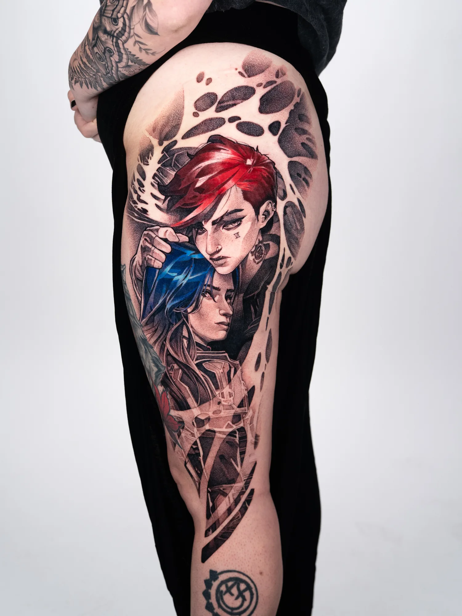 Detailed color tattoo on thigh featuring two stylized figures with red and blue hair.