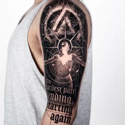 Tattoo featuring a central figure, geometric shapes, and bold lettering on the arm.