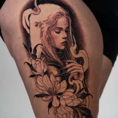 Black and grey tattoo on the right thigh of a Manon Blackbeak from the Throne of Glass series with her eyes closed and head bowed, one hand at her chest, framed by magnolias and dark ribbons of smoke.