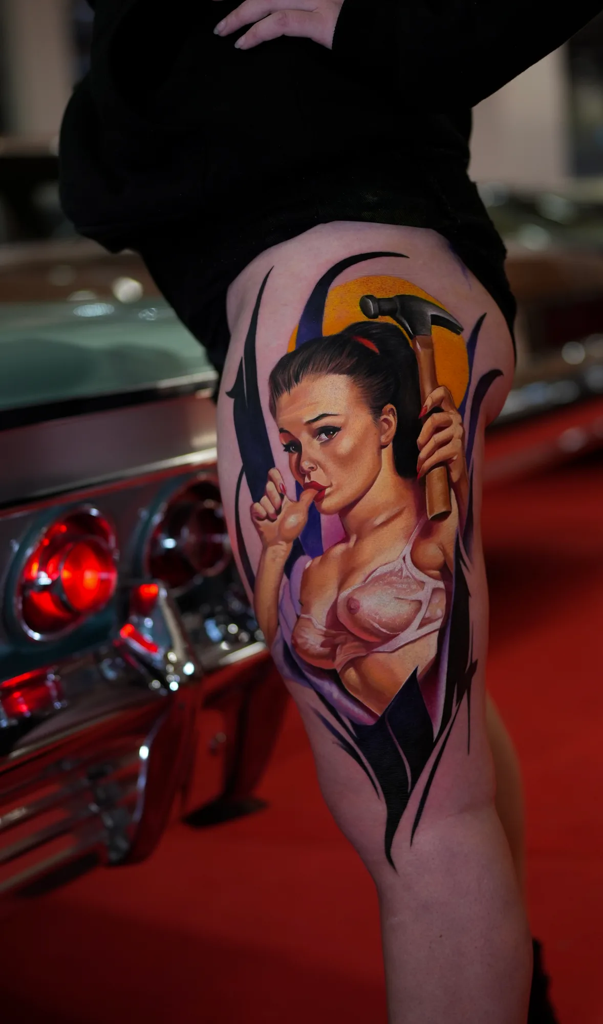 Tattoo of a pin-up woman holding a hammer on upper thigh.