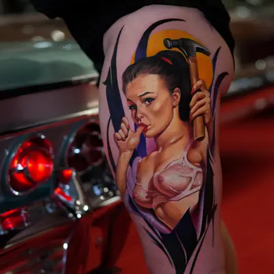 Tattoo of a pin-up woman holding a hammer on upper thigh.