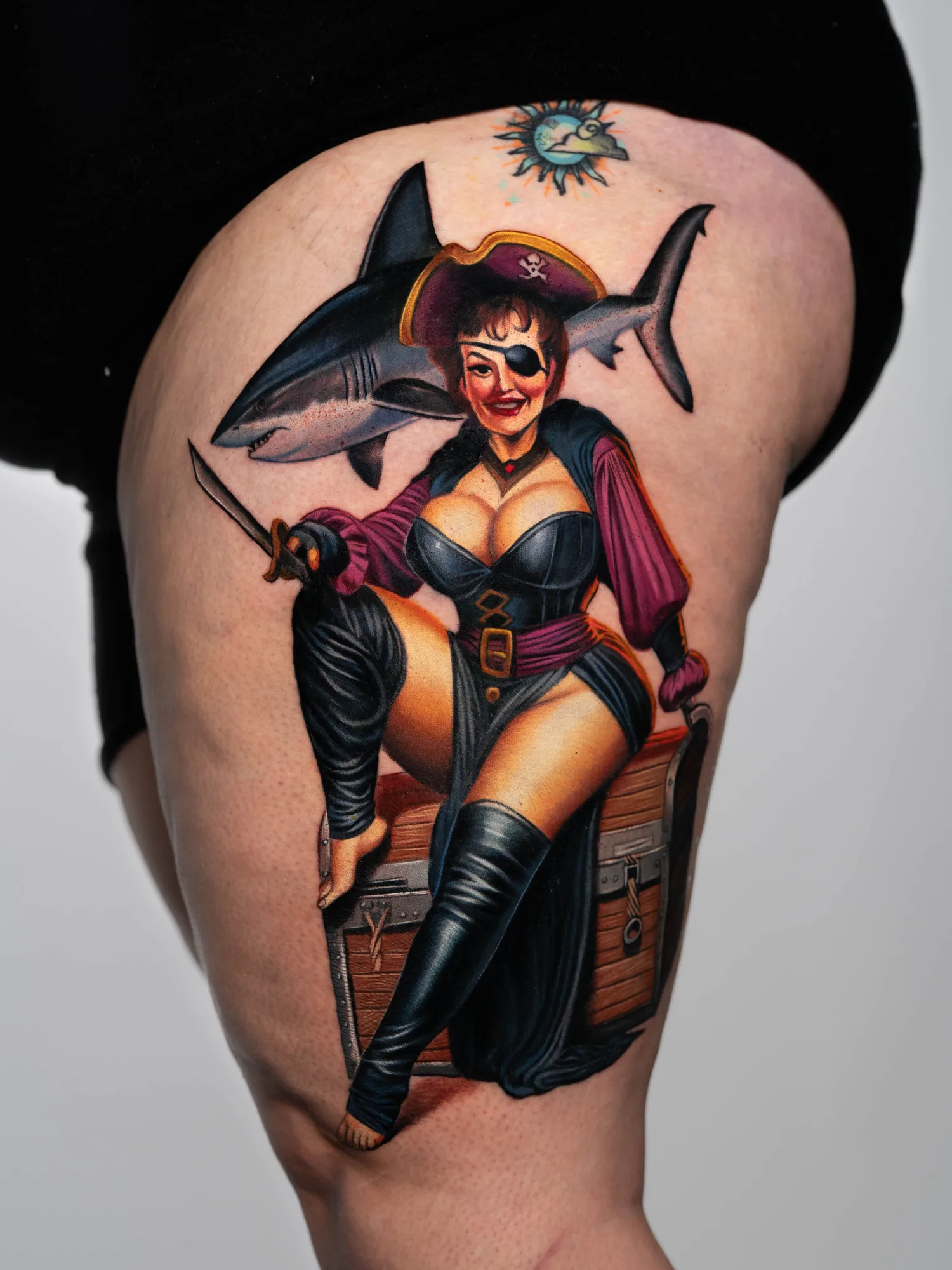 Colorful tattoo of pirate woman with shark and treasure chest on thigh.