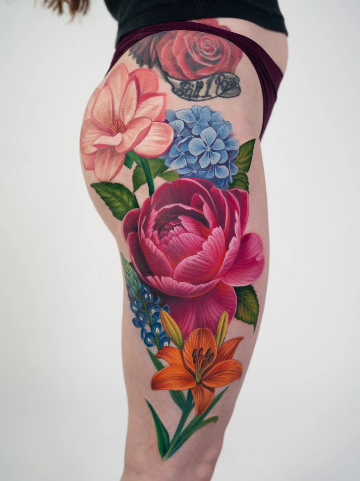 Vibrant floral tattoo on thigh featuring various colorful flowers.