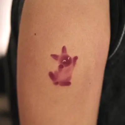 Small tattoo of a pink cartoon character on an arm.