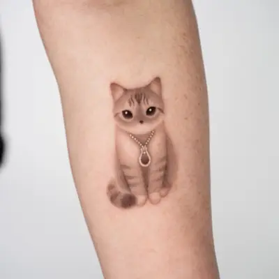 Tattoo of a realistic cat with a necklace on an arm.