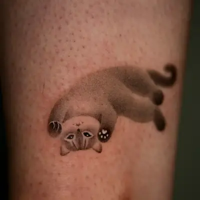 Tattoo of an upside-down cat in minimalist style on skin.