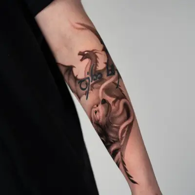 Forearm tattoo of a dragon and wolf with script.