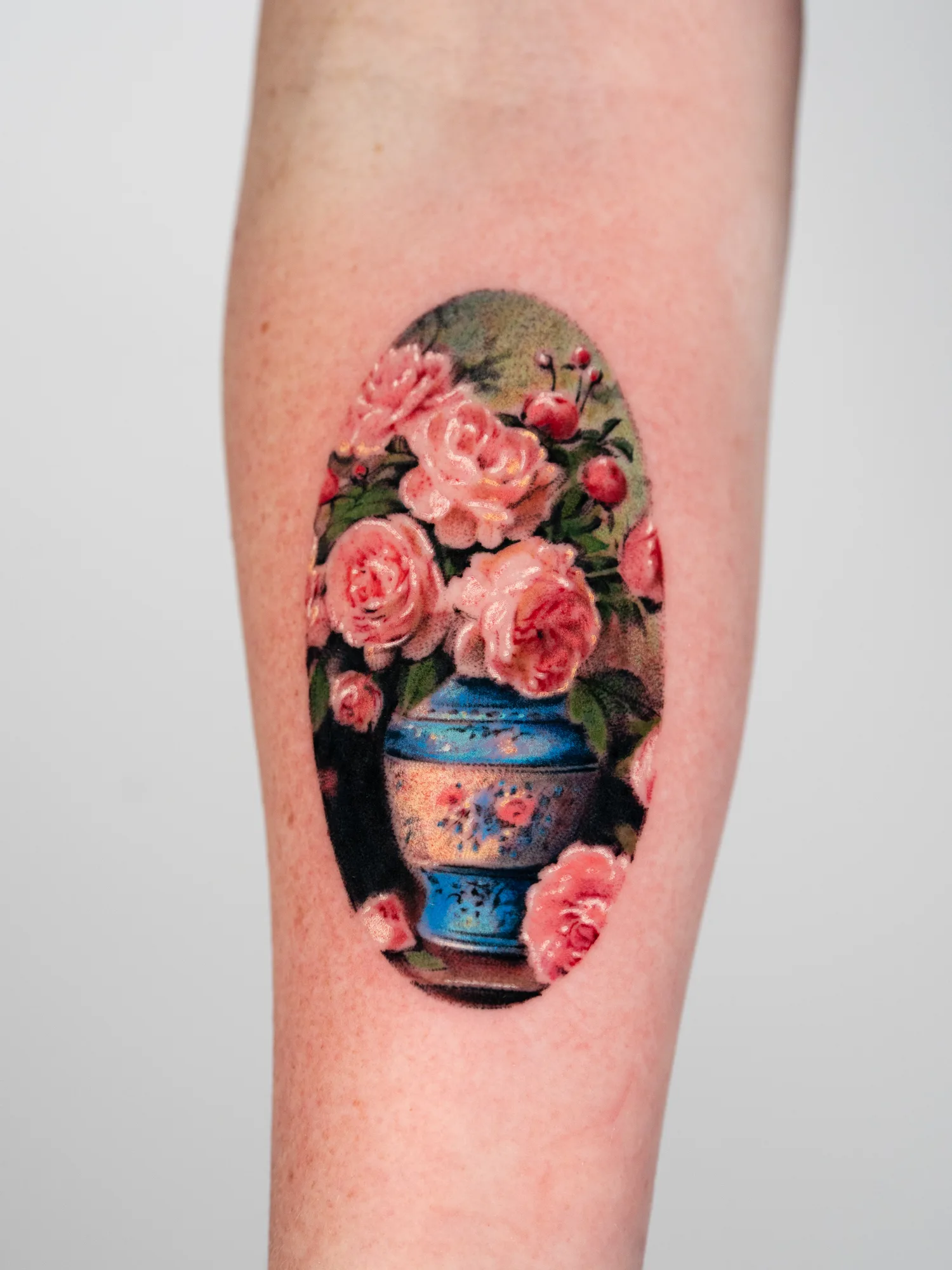 Tattoo of a blue vase with pink peonies on an arm.