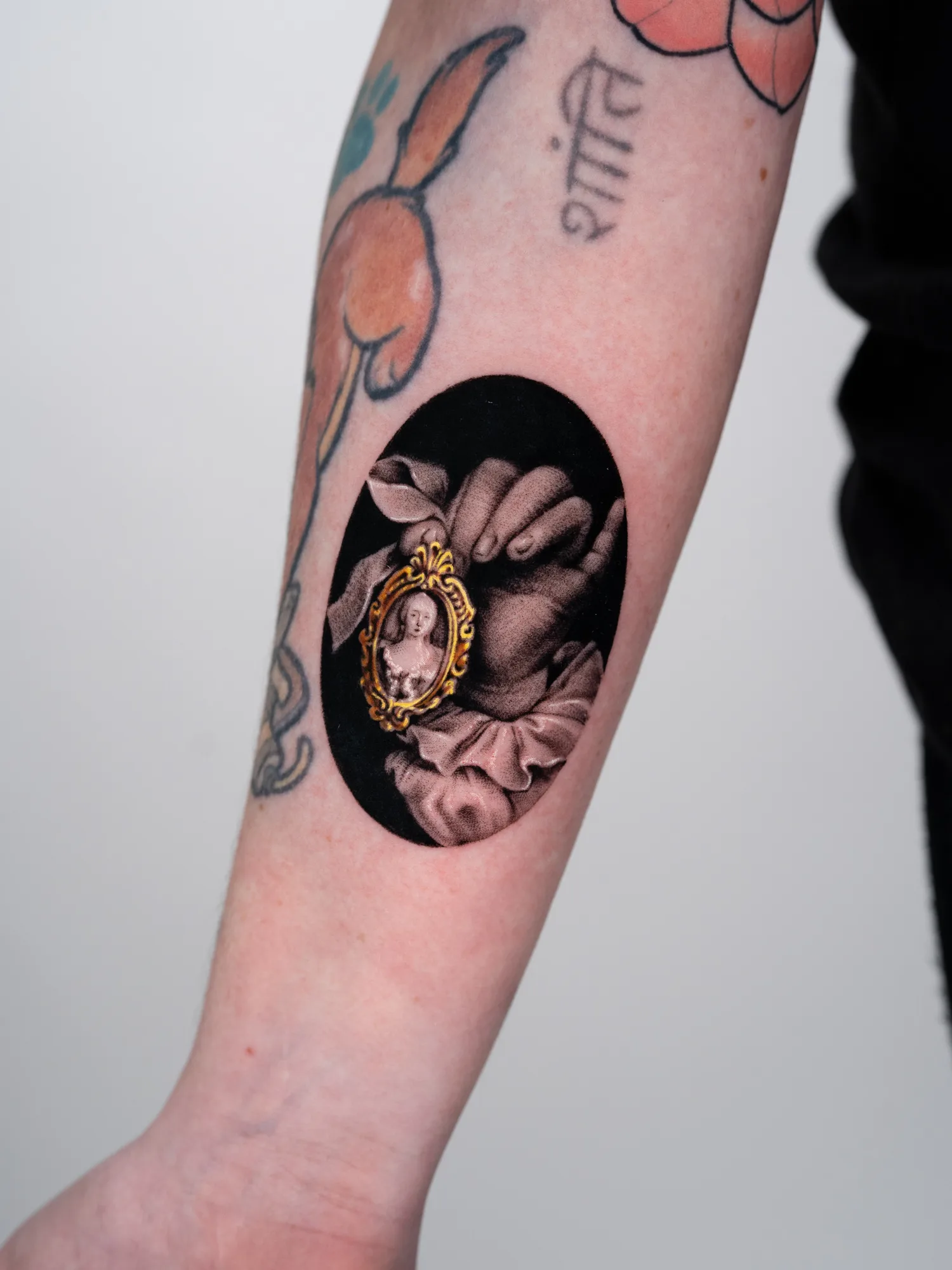 Black ink tattoo of a hand holding a small portrait inside a decorative frame.