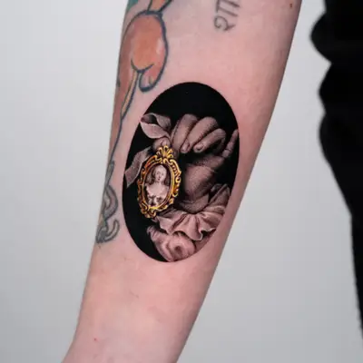 Black ink tattoo of a hand holding a small portrait inside a decorative frame.