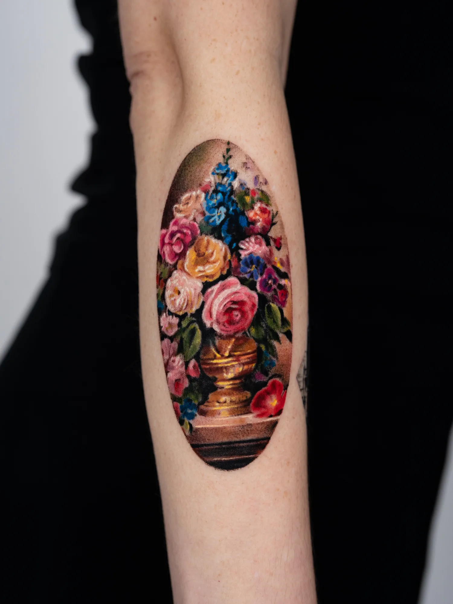 Realistic floral tattoo of a vase with flowers on a forearm.