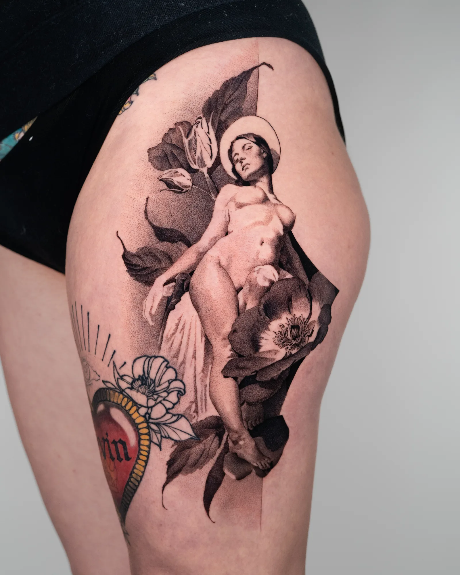 Tattoo of a nude figure with floral elements on a thigh.