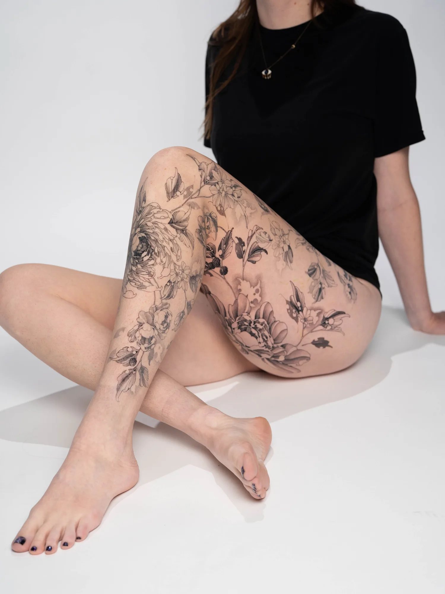 Black and grey floral tattoo covering woman's leg and thigh
