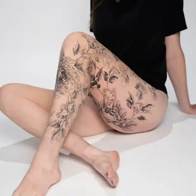 Black and grey floral tattoo covering woman's leg and thigh