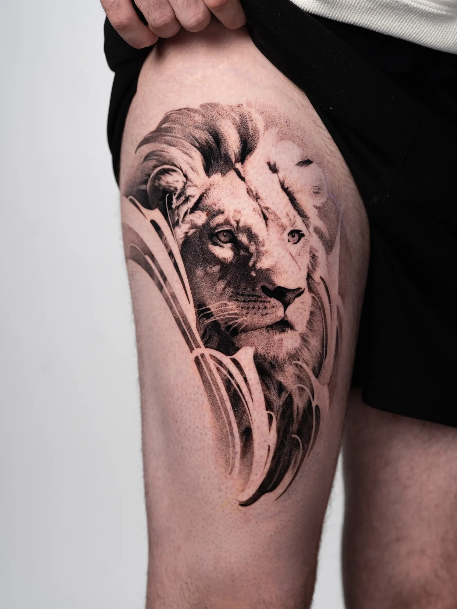 Tattoo of a lion's head on thigh in black and grey style