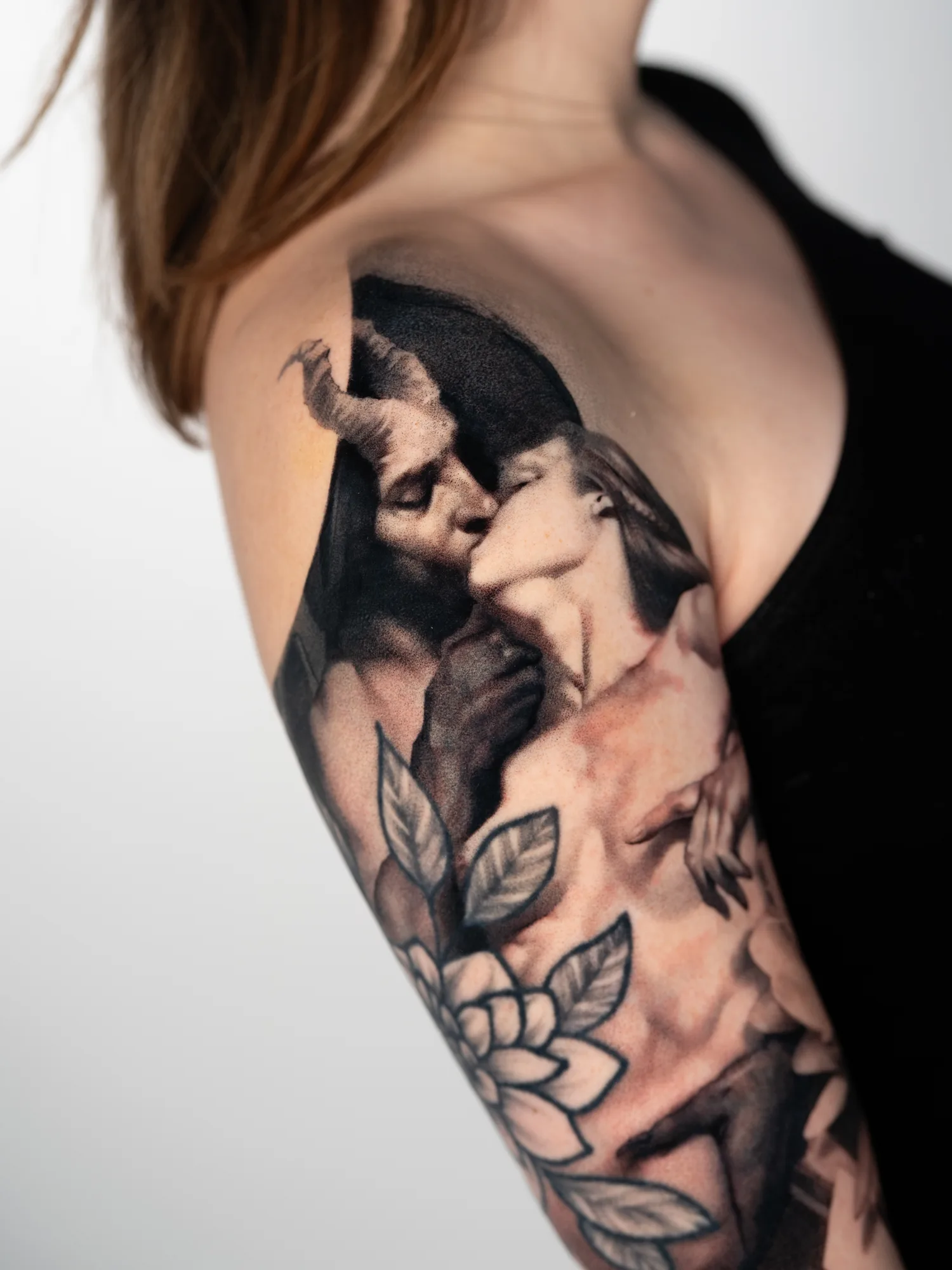 Tattoo of a couple kissing with floral elements on upper arm