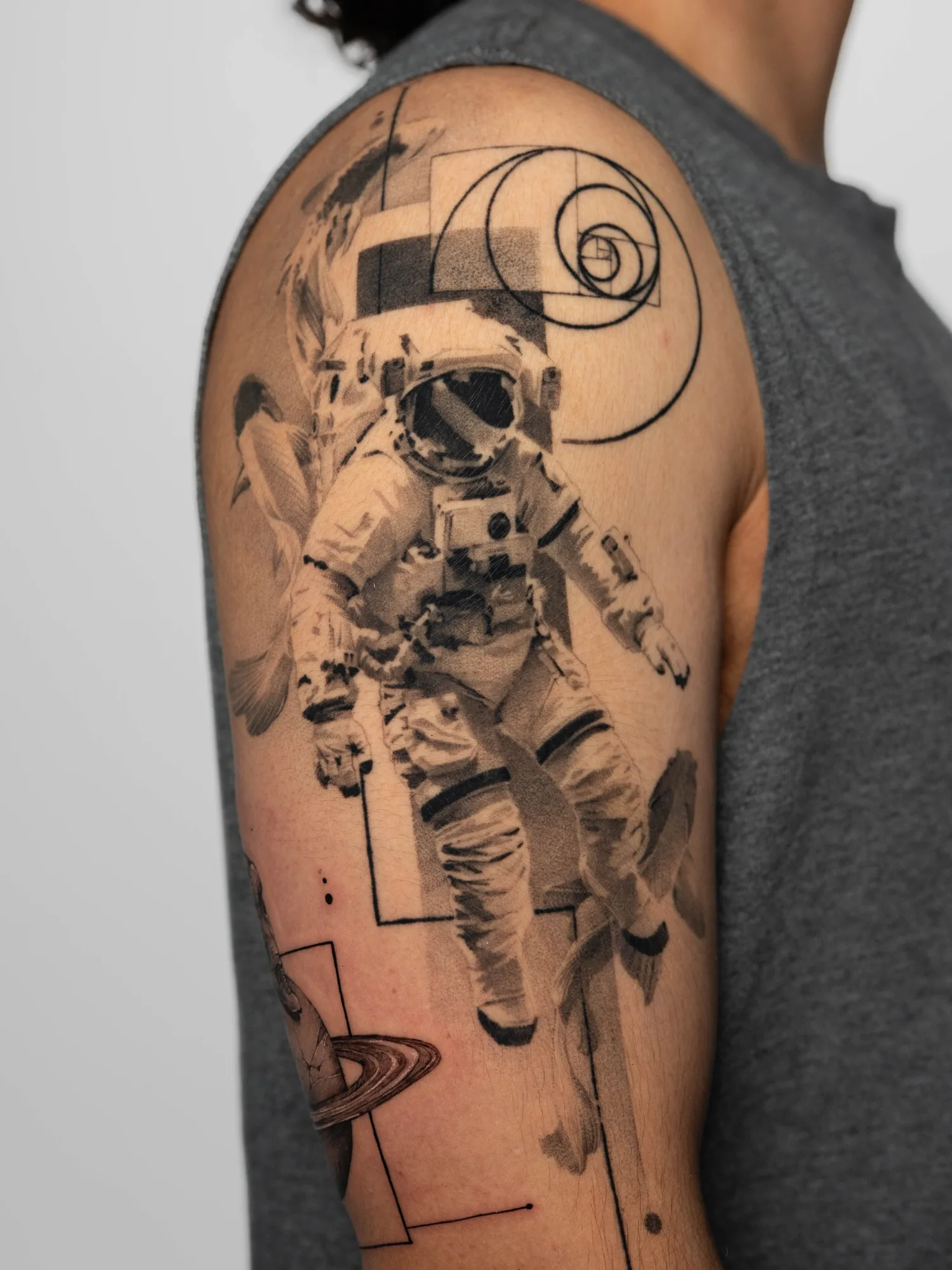 Black and grey realism tattoo of an astronaut and koi fish with fine line geometric elements.