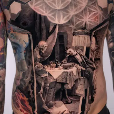 Black and grey stipple tattoo across a stomach showing a skeleton seated at a dinner table with a man in a tuxedo asleep in his chair beside it, a fringed lamp above, framed by a curtain and the sacred geometry pattern across the chest.
