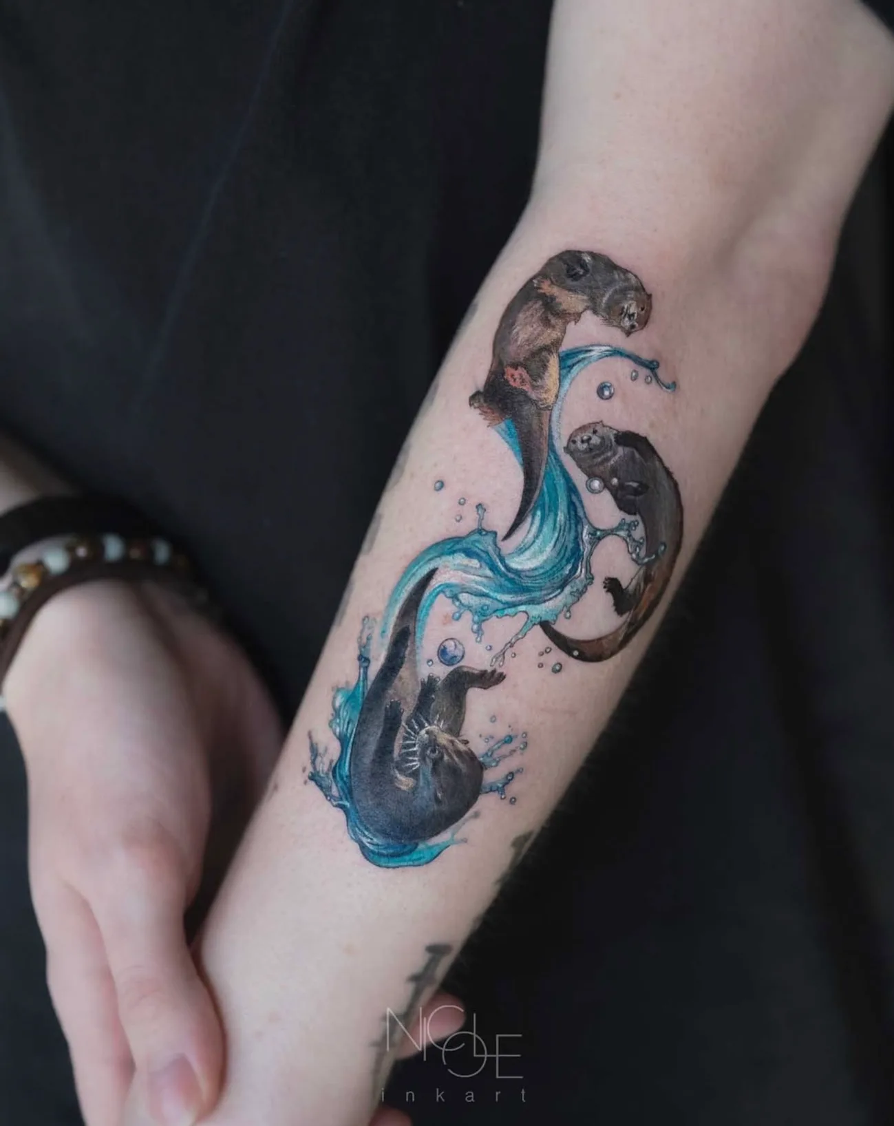 Tattoo of two otters and water on forearm