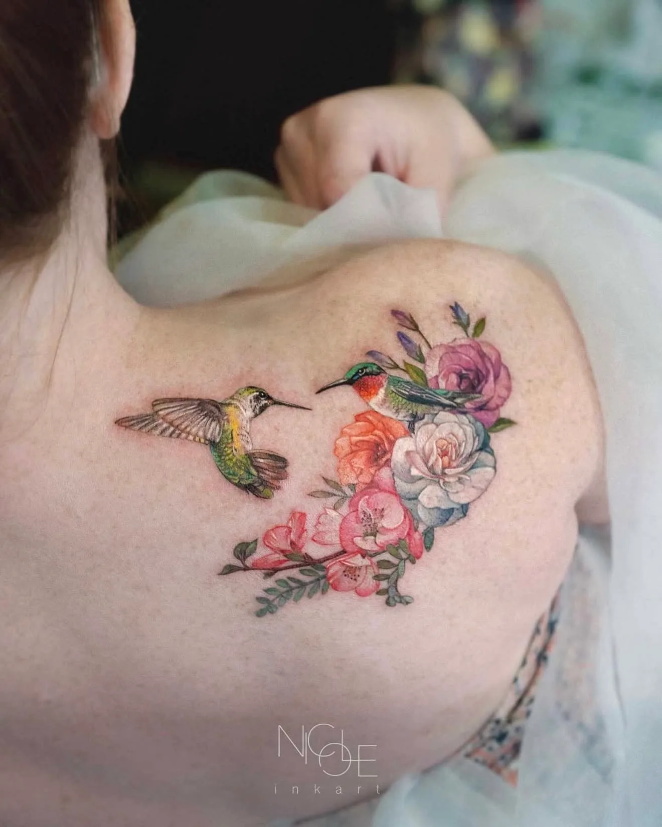 Tattoo of two hummingbirds and colorful flowers on shoulder.