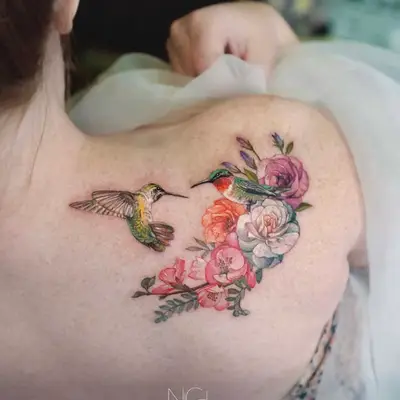 Tattoo of two hummingbirds and colorful flowers on shoulder.