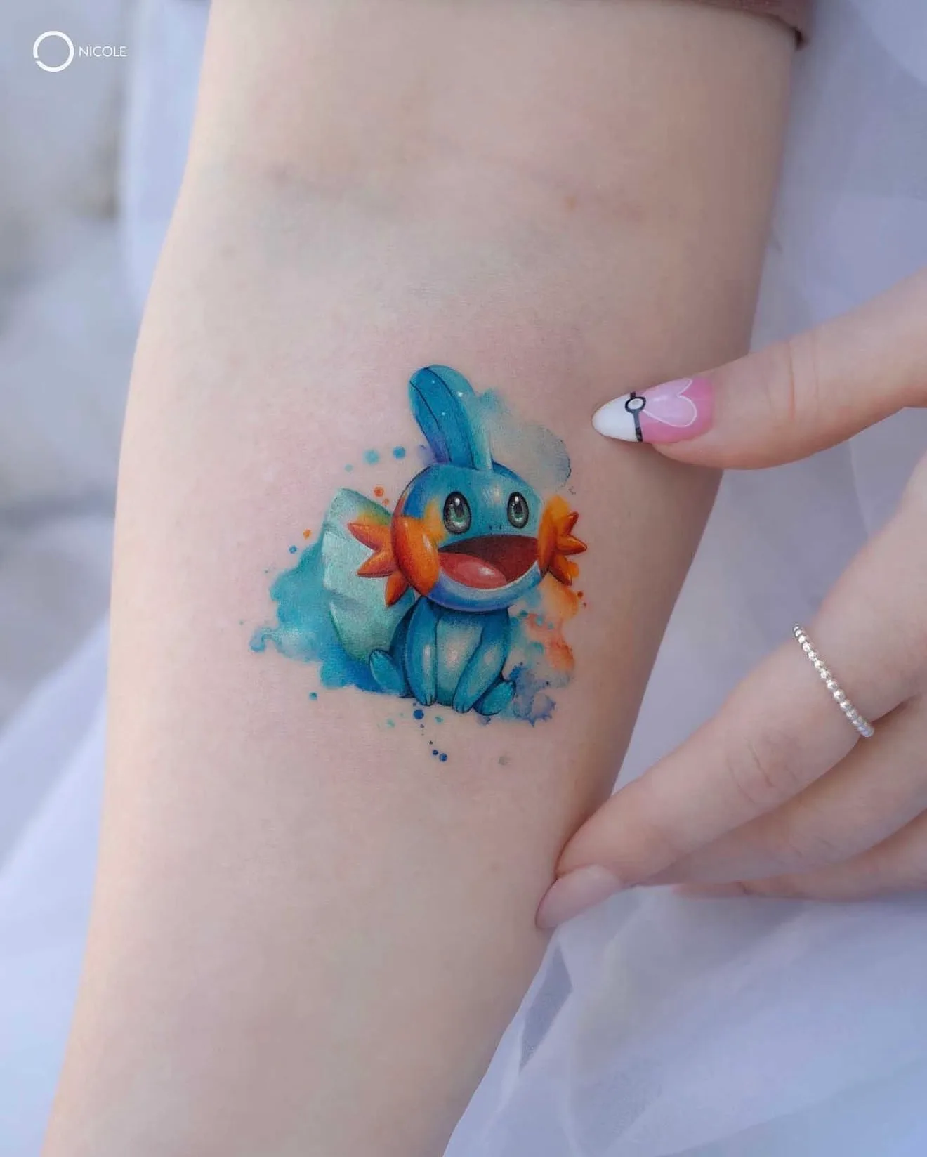 Colorful tattoo of Mudkip on inner arm with watercolor effect.