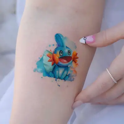 Colorful tattoo of Mudkip on inner arm with watercolor effect.
