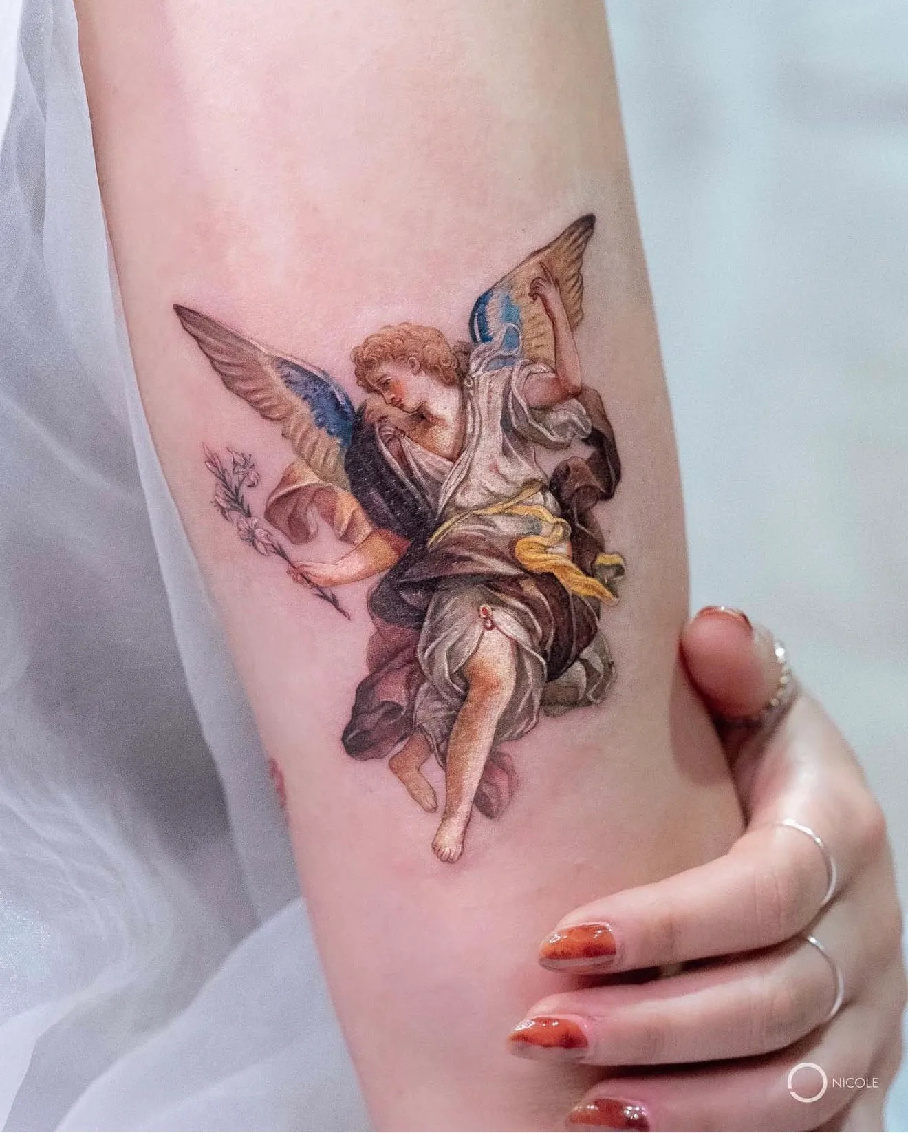 Tattoo of an angel with detailed wings holding flowers.