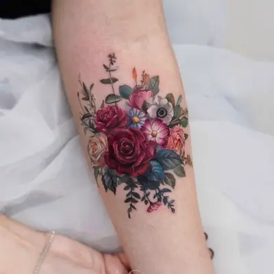 Floral tattoo with roses and various flowers on forearm.