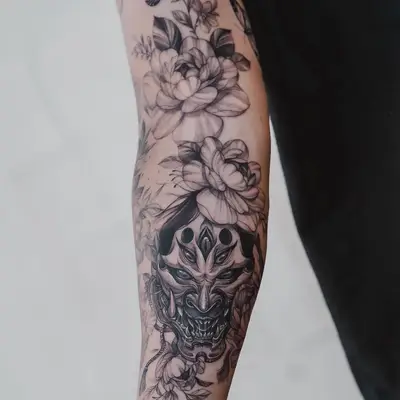 Tattoo of floral designs and a demon mask on the forearm.