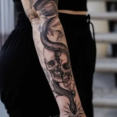 Black and grey tattoo of a snake entwined with a skull on forearm.