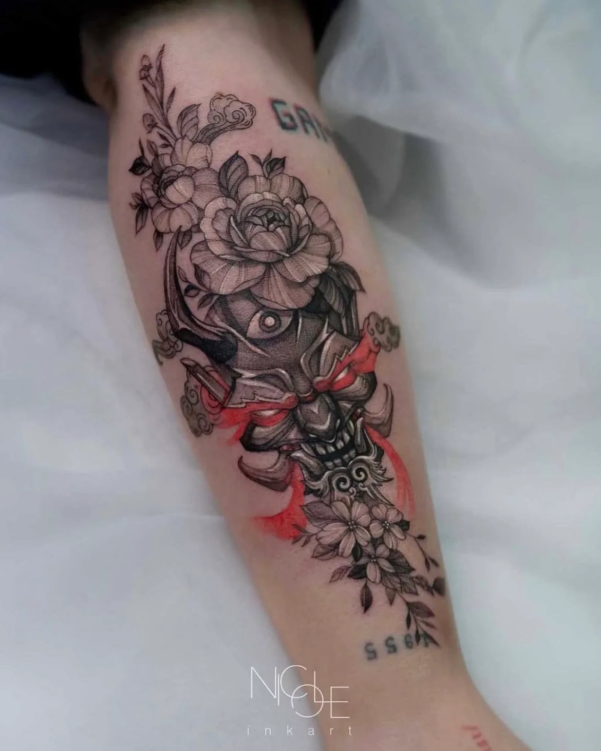 Tattoo of a hannya mask with floral and watercolor elements on forearm.