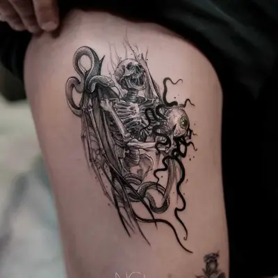 Tattoo of a skeleton entwined with a tentacled eyeball on upper thigh.