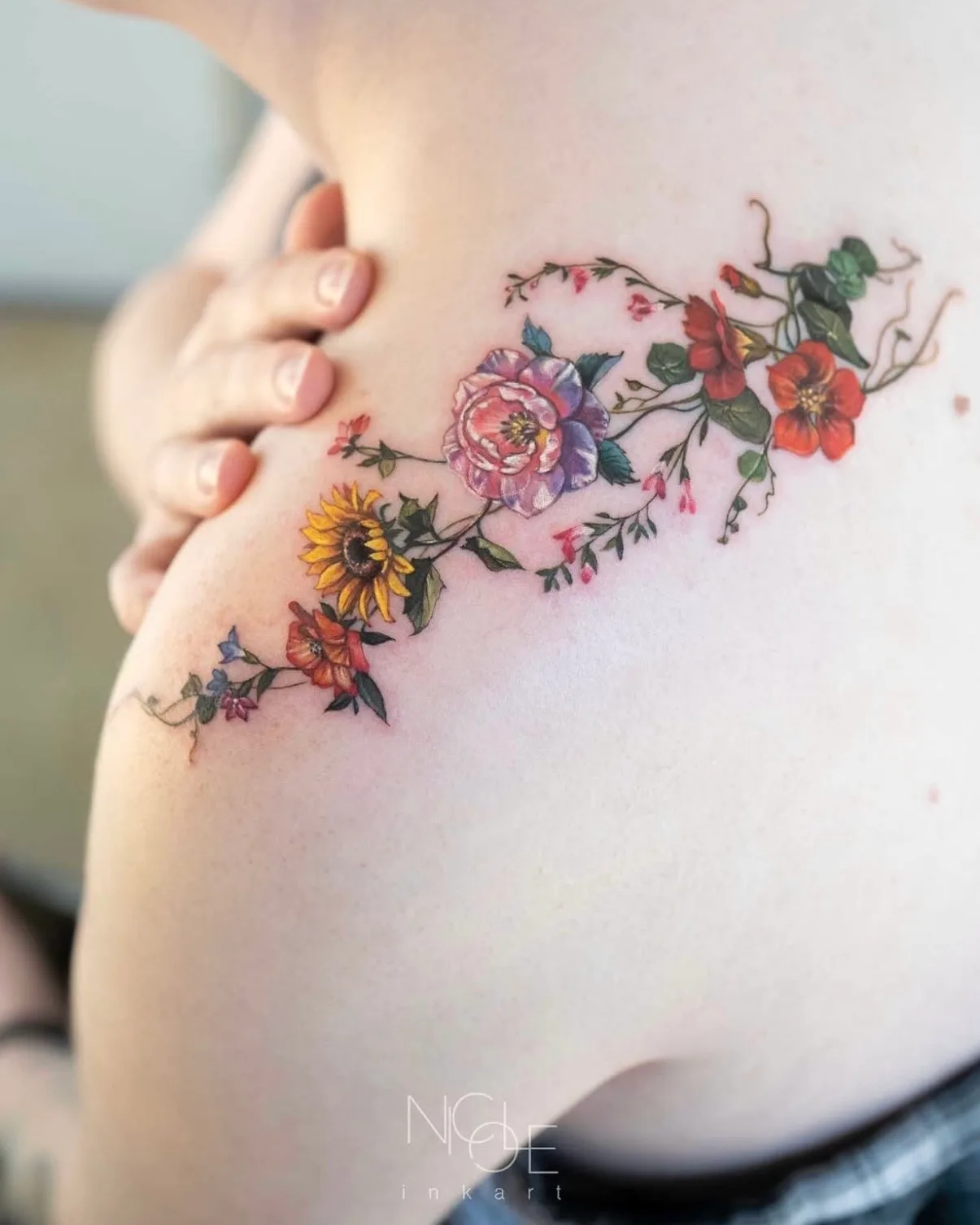 Colorful floral tattoo on upper arm with various flowers.