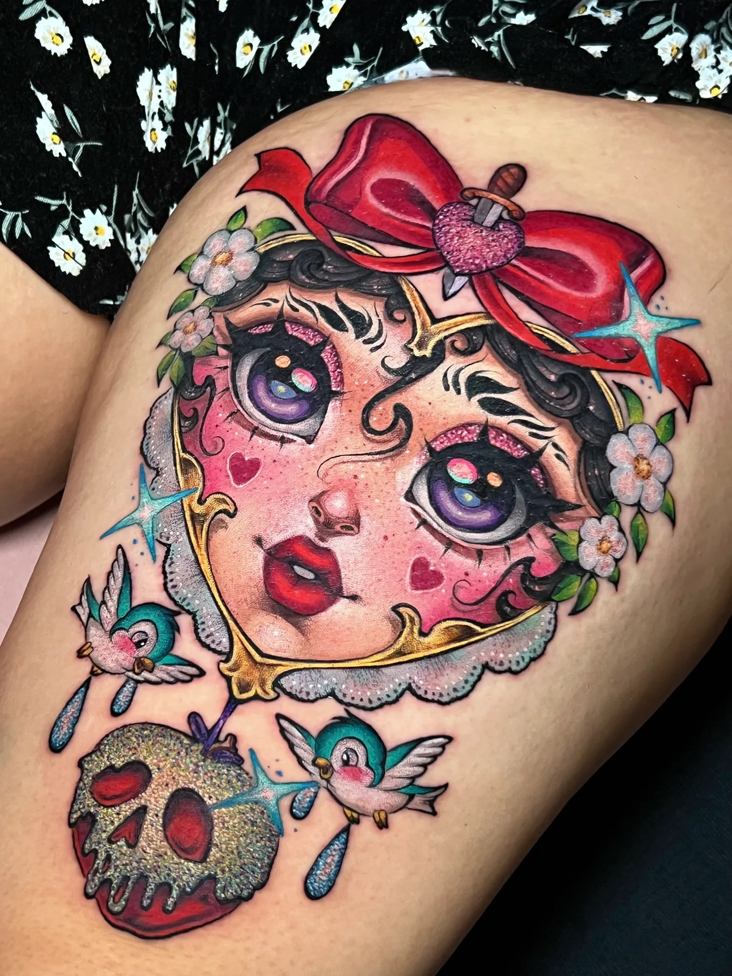 Colorful tattoo of a face with a bow, floral accents, birds, and a glittery skull.