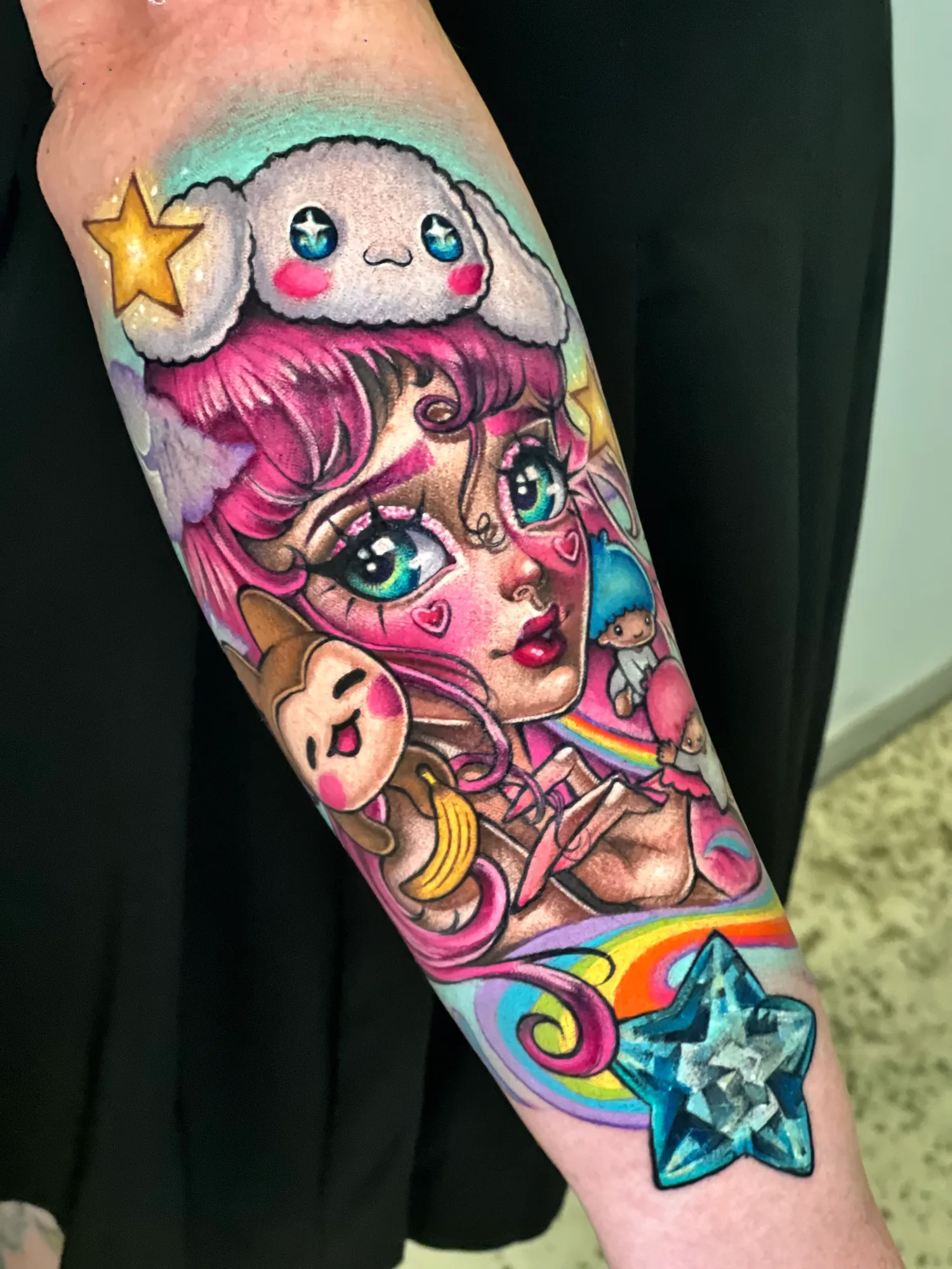 Color tattoo on a forearm of a pink-haired anime-style girl wearing a white Sanrio character as a hat, with small Sanrio characters, a rainbow and a faceted blue star near the wrist