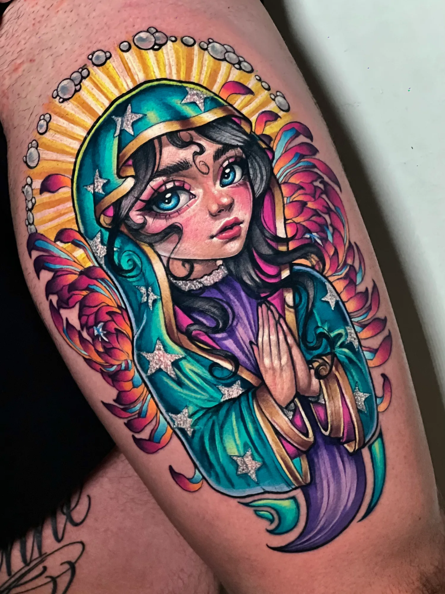 Tattoo of a stylized woman with colorful robes and hands in prayer.
