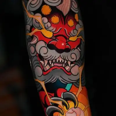 Japanese style tattoo of a fierce, colorful oni mask with vivid patterns on an arm.