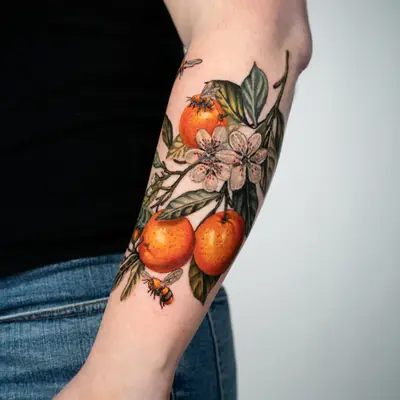 Colorful tattoo of oranges, blossoms, and bees on forearm.