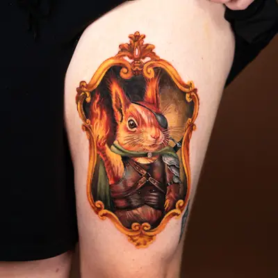 Colorful tattoo of a squirrel in a Renaissance-style frame on the thigh.