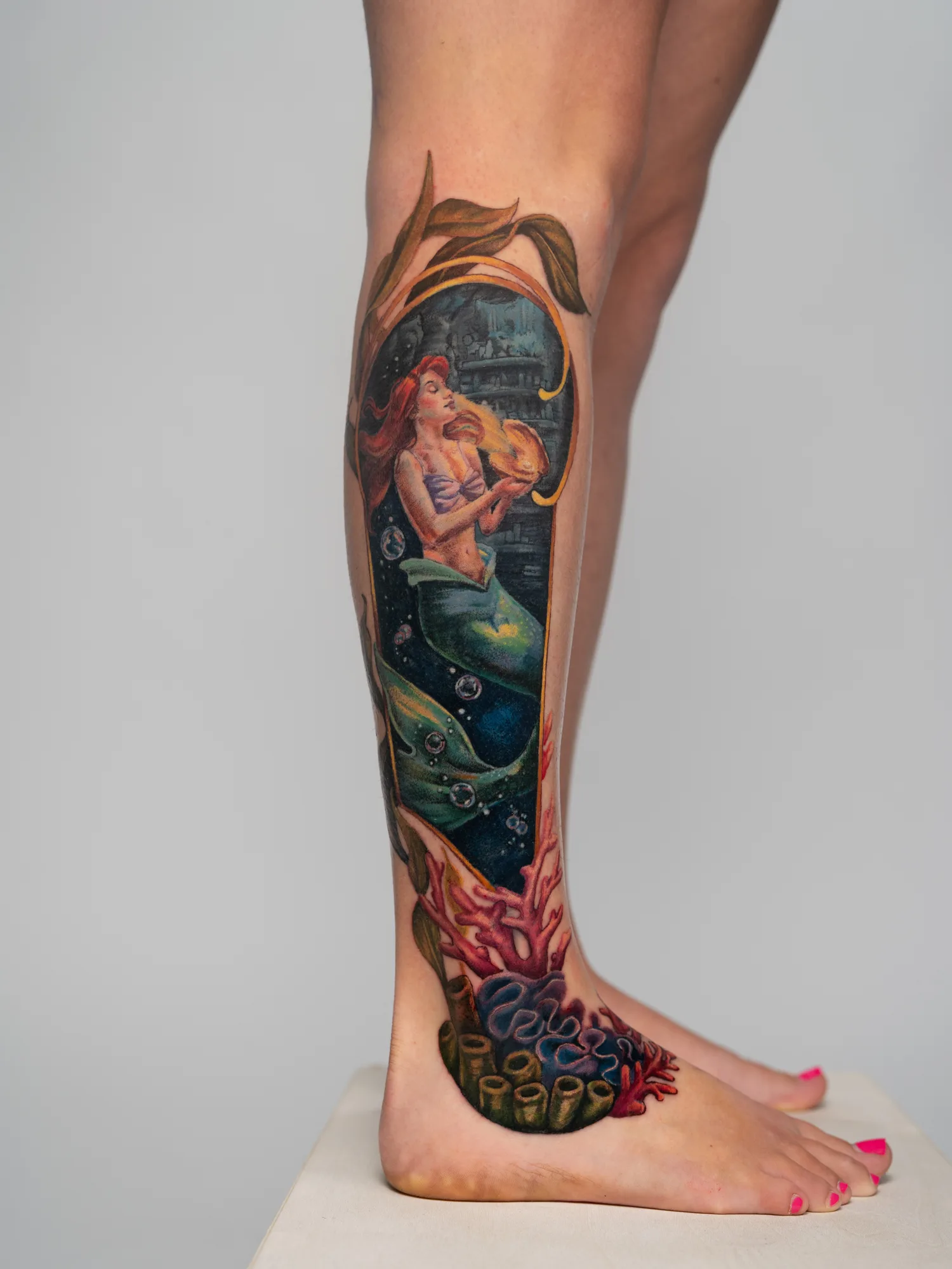Tattoo of a mermaid holding a seashell on leg.