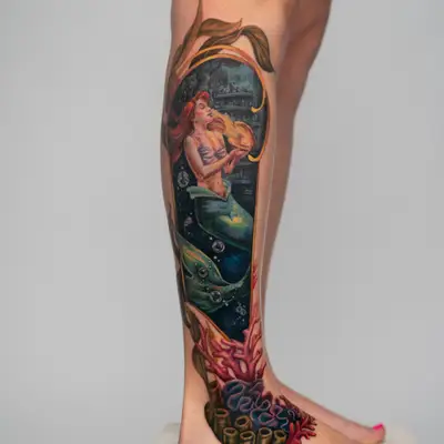 Tattoo of a mermaid holding a seashell on leg.