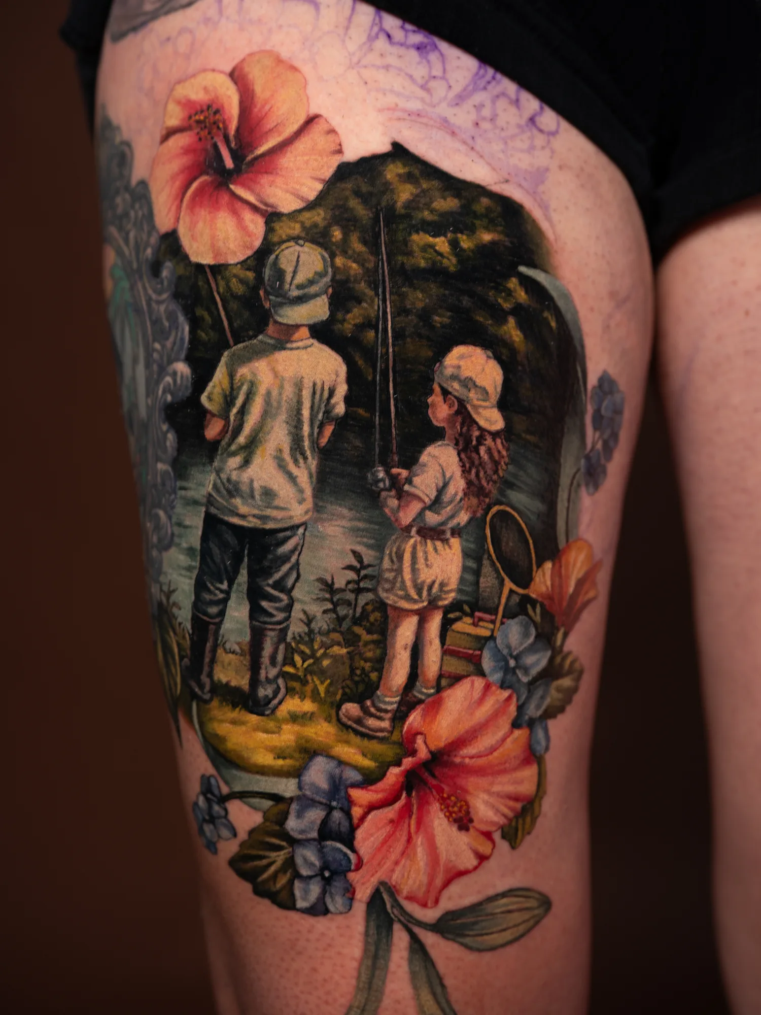 Tattoo of two children with fishing rods surrounded by flowers.