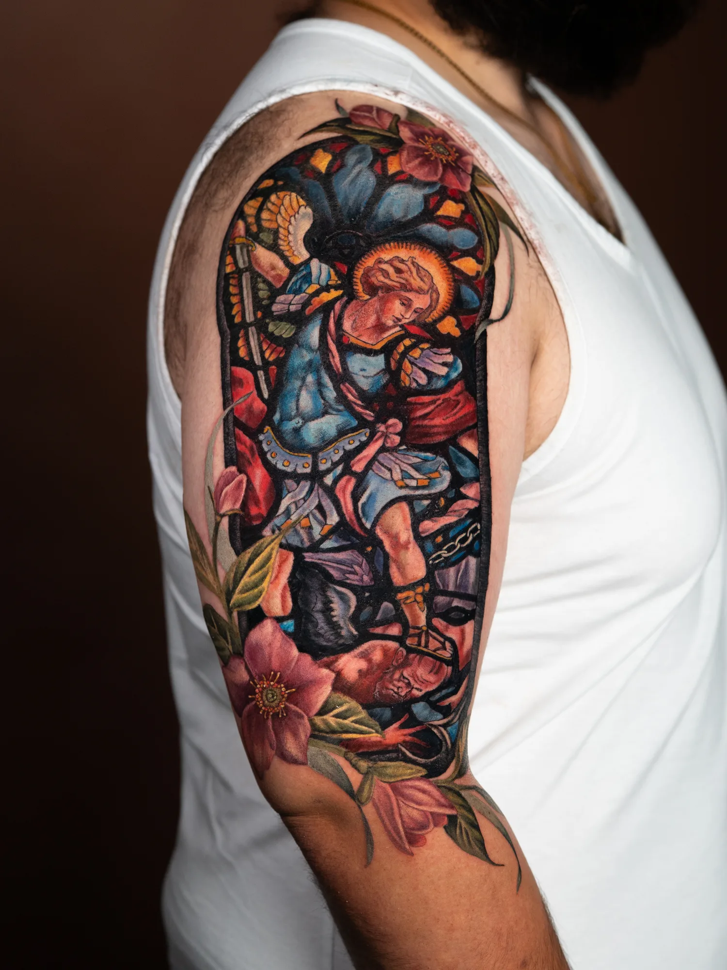 Colorful arm tattoo of an angel with floral and stained glass elements.