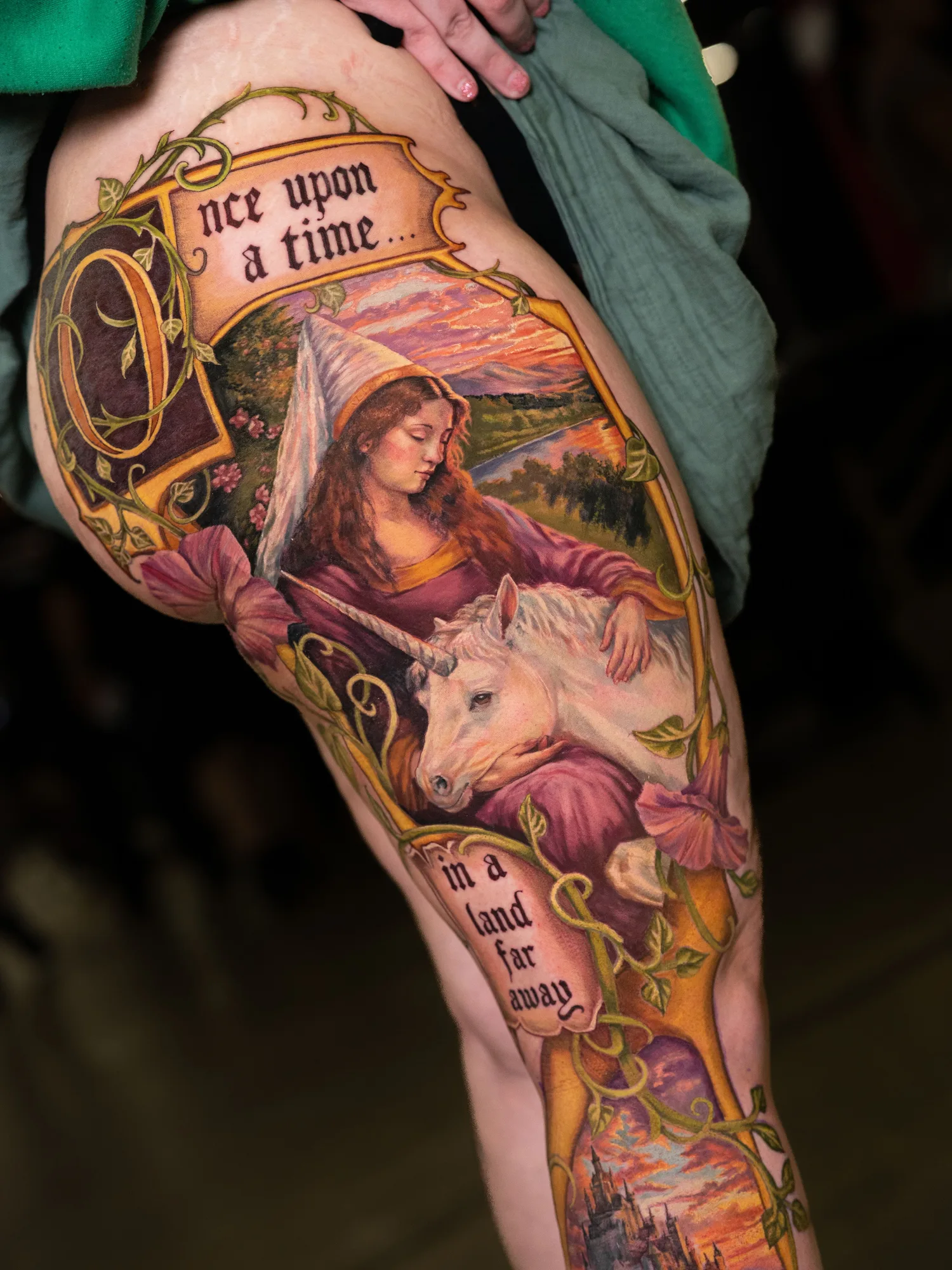 Color painterly tattoo of a maiden in a pointed hennin embracing a white unicorn, framed by an illuminated Once Upon A Time banner, on a leg panel.