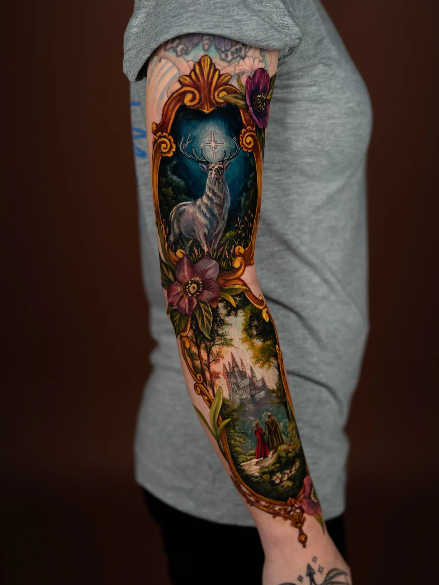 Color painterly sleeve of two framed scenes, a white stag under a star and a castle with two robed figures, joined by gold frames and hellebores, on an outer arm.