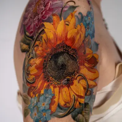 Color realism tattoo of a large sunflower with a bee, a magenta chrysanthemum and forget-me-nots, wrapping a shoulder cap.