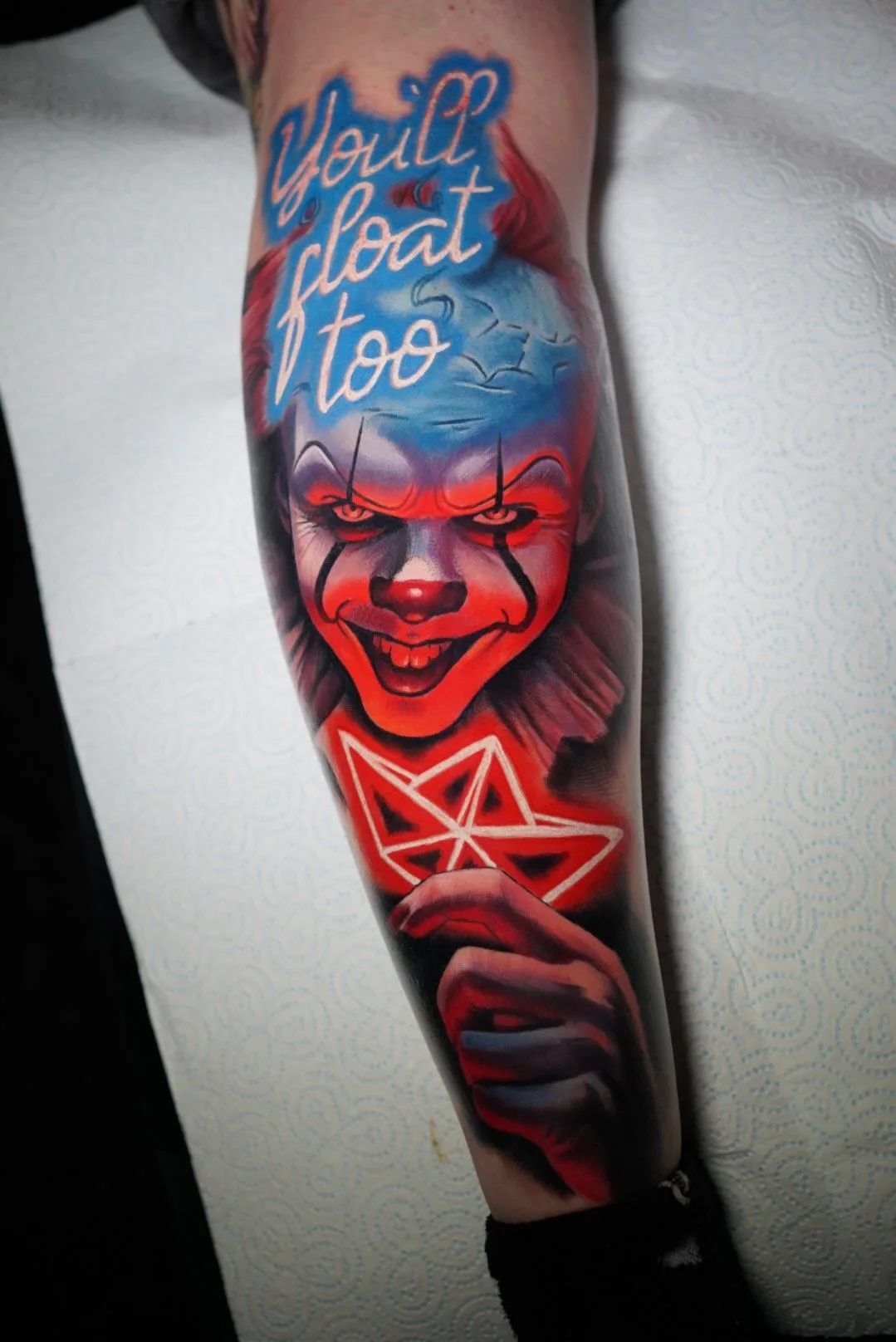 Tattoo of Pennywise on a calf holding a neon paper boat.